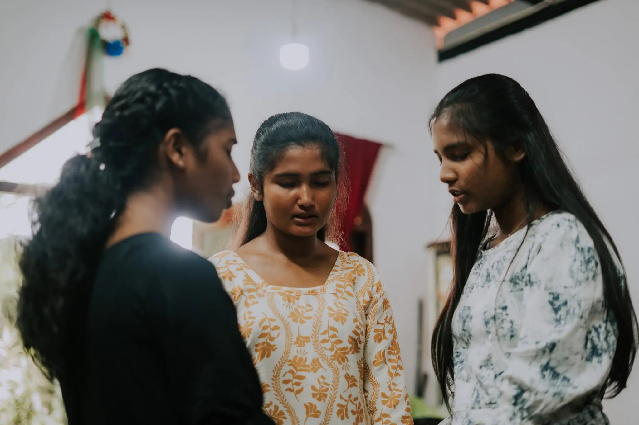 Three young women standing side by side with heads bowed