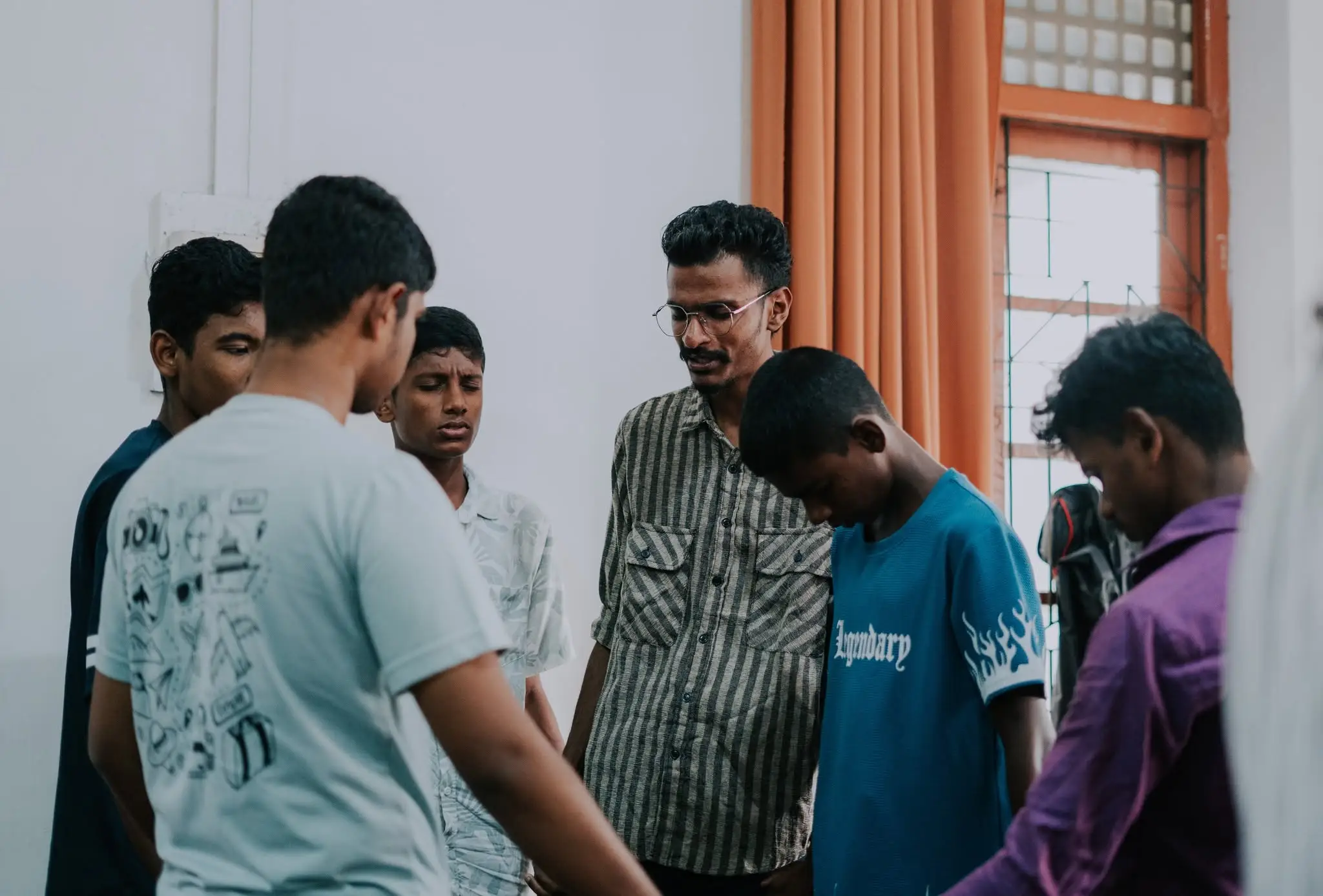 A group standing in a circle with heads bowed, praying together